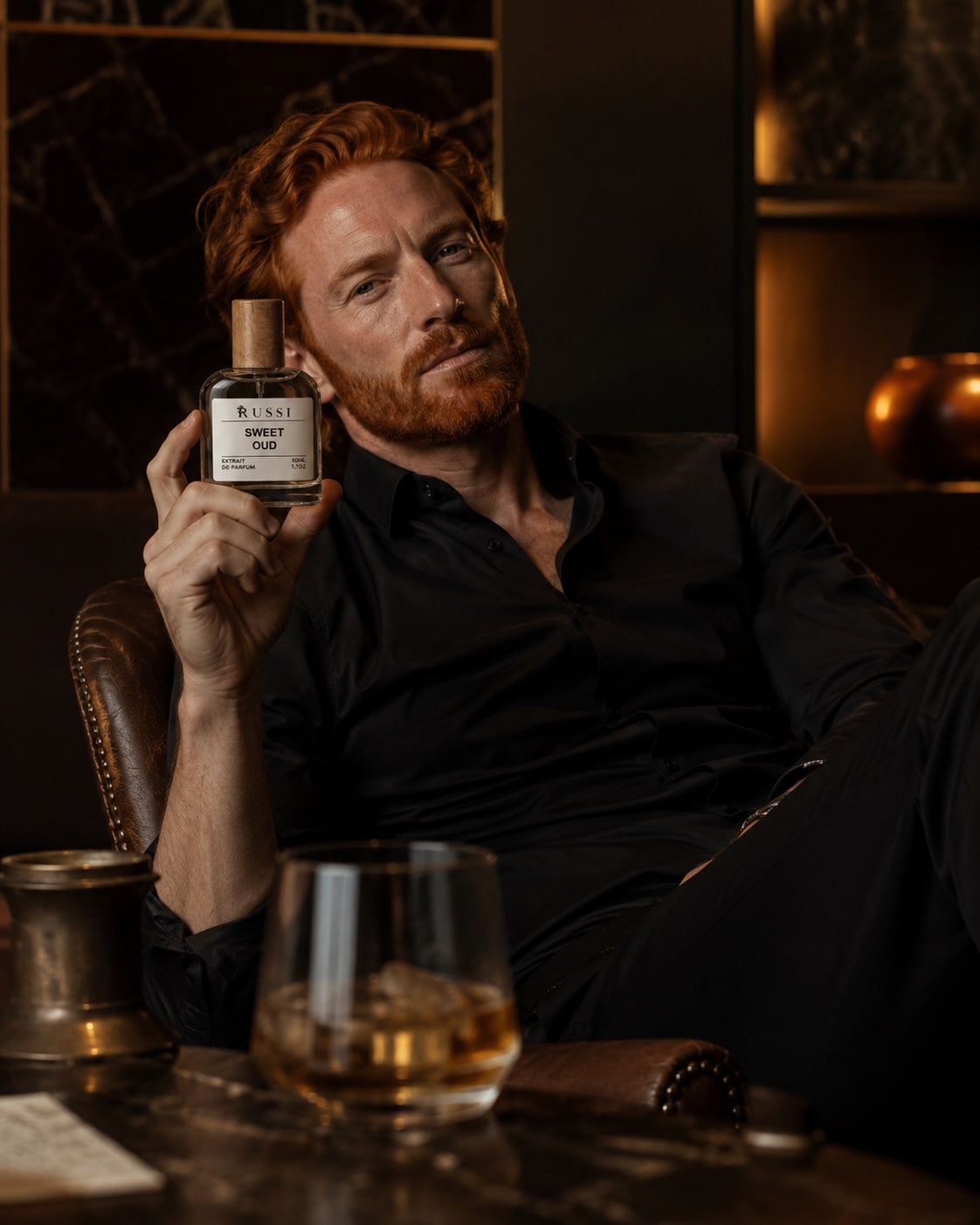 SWEET OUD perfume held by a red-haired man in a dark luxury interior